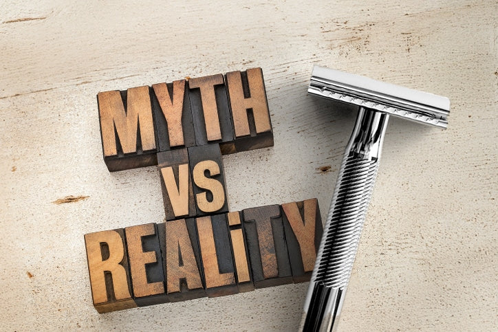 Wooden letter blocks spelling out 'MYTH VS REALITY' next to a chrome safety razor on a light wood surface