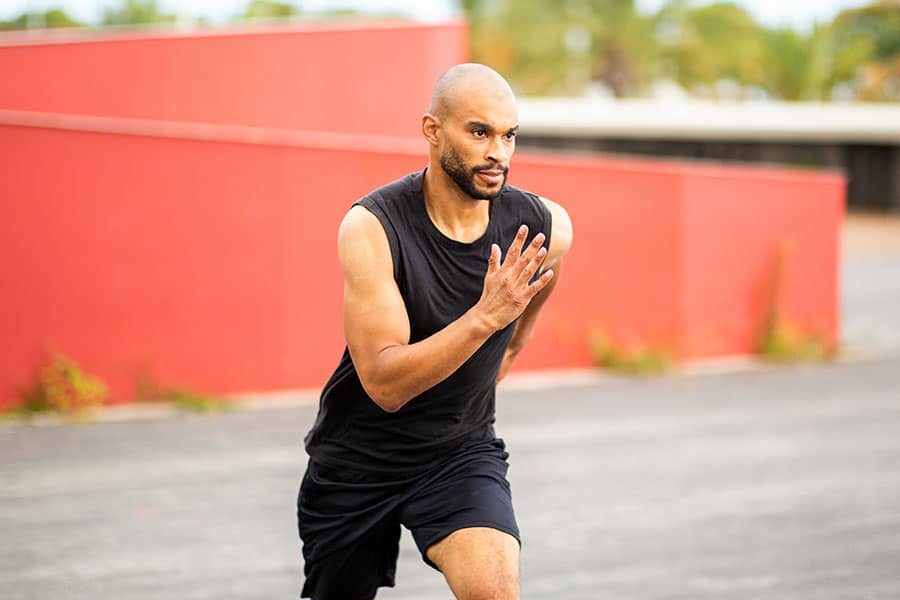 A bald man with a beard running outdoors in athletic clothes, appearing to be mid-workout