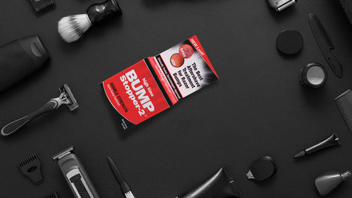 image of Bump Stopper-2 on a black background surrounded by barber grooming products including a razor, electric razor, brush, cob, and electric razor accessories
