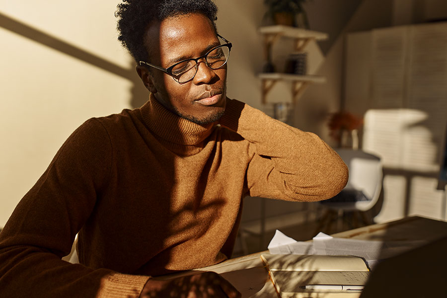 Stressed young dark-skinned male with glasses, massaging his neck.