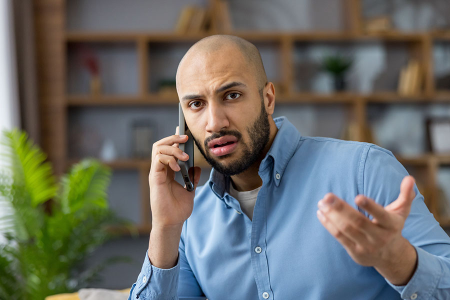 A bald man making a phone call with a frustrated look on his face.